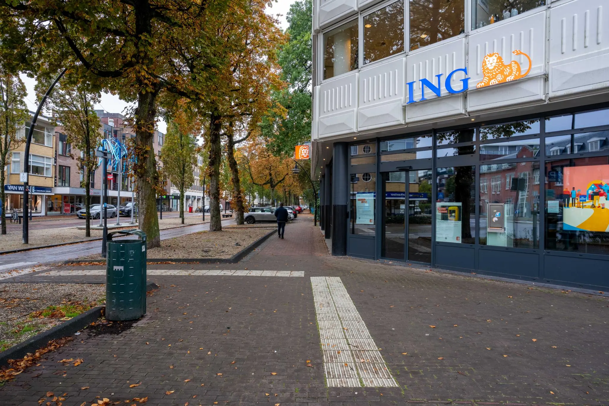 Vooraanzicht van een ING-bankfiliaal aan de 1e Hogeweg met herfstige bomen en winkels in de straat.